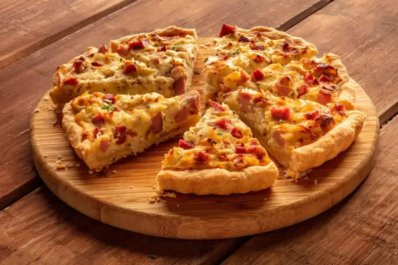 Fette di torta salata patate e salsiccia dorata e invitante, servite su un tagliere di legno.