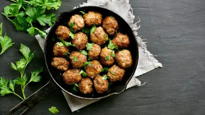 Polpette al forno dorate e succulente, guarnite con prezzemolo fresco, in una padella di ghisa su sfondo scuro.